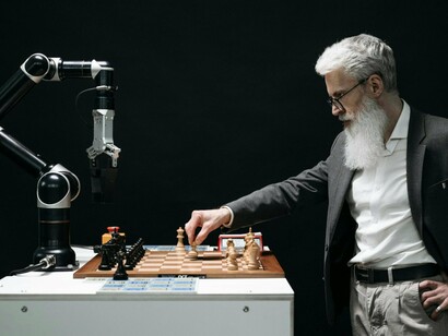 A human player facing a robotic opponent across a chessboard, reflecting the challenge of maintaining relevance in an AI-driven world