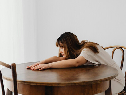 A woman leaning on a table, quiet grief marked by an empty chair