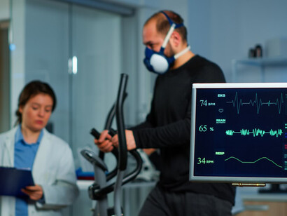 A team of medical researchers monitoring the VO2 performance of a man during a run, wearing a mask, while an EKG scan runs on the computer screen in the laboratory