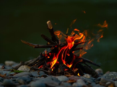 A small campfire glowing by a river, representing the warmth of shared wisdom passed from one generation to the next