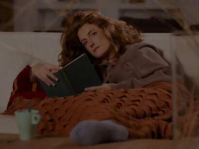 Enveloped in the comfort of winter, a woman dressed in cozy attire sits on a couch, immersed in a captivating book
