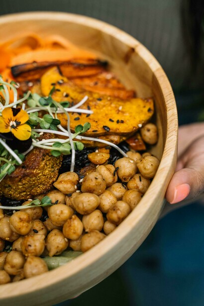 Person holding a wooden bowl filled with cooked, wholesome food
