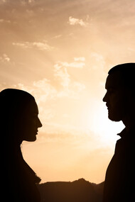Silhouette di un uomo e una donna che si guardano, con un cielo al tramonto dai colori caldi sullo sfondo
