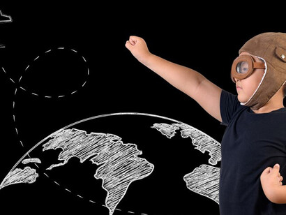 Against a black wall decorated with white drawings, a boy pretends to be a superhero, vividly demonstrating his creativity and playful spirit