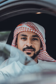 A man in a white long-sleeve shirt, wearing a red and white hijab, sitting inside a car