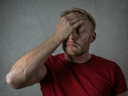 A man with closed eyes touching his forehead in confusion