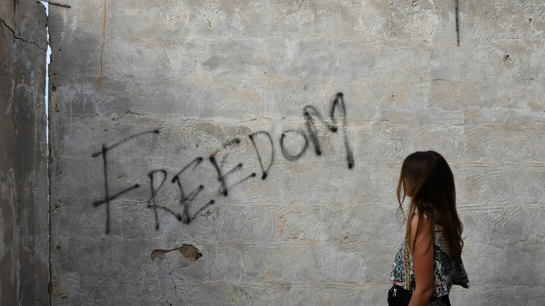 A woman stood in front of graffiti on a wall. Social justice and peace need to be central topics for all governments and international institutions