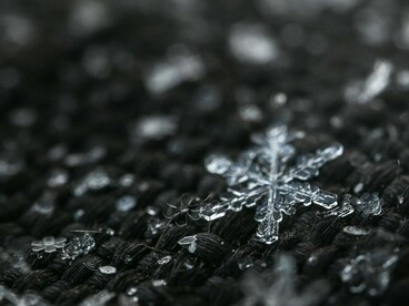 A single, perfectly formed snowflake stands out against a blurred background of other ice crystals, embodying the detailed artistry often associated with winter's frozen precipitation