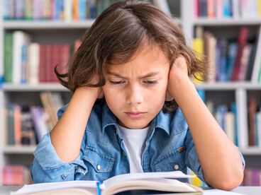 A child sitting at a desk, staring at schoolwork with visible frustration, representing the growing challenge of sustained attention in a distracted age