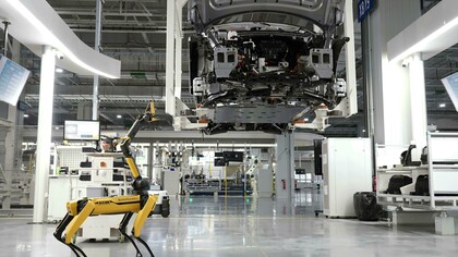 Un robot quadrupede di Boston Dynamics ispeziona una linea di assemblaggio automatizzata in una fabbrica high-tech, simbolo della trasformazione postindustriale e della crescente automazione dei processi produttivi