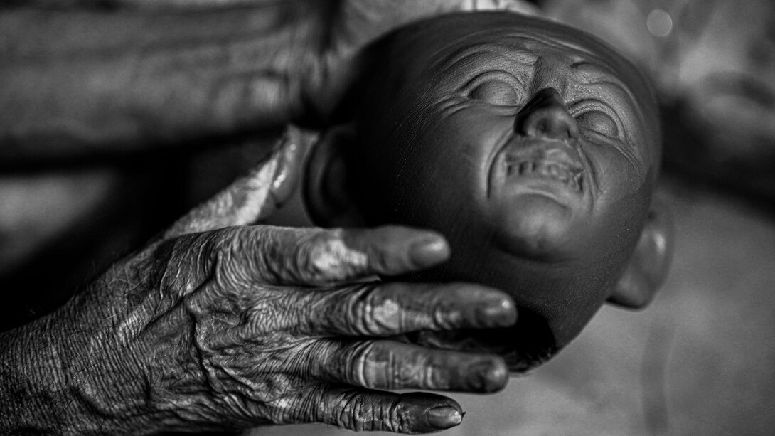 Um artesã idosa modela uma cabeça em argila, trabalhando cuidadosamente os volumes e os detalhes da escultura. Em suas mãos, a matéria ganha forma por meio de gestos que exigem prática, sensibilidade e paciência. Assim como no acordelado, a cerâmica artesanal preserva conhecimentos transmitidos pela experiência e transforma o trabalho manual em expressão artística
