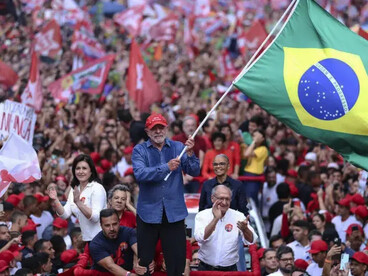Lula segura a haste de uma grande bandeira do Brasil, que ocupa boa parte do primeiro plano, enquanto apoiadores se aglomeram atrás dele, exibindo bandeiras e acompanhando a manifestação. A composição aproxima a figura do presidente da multidão e coloca o símbolo nacional no centro da cena. Em um país marcado pela disputa política em torno dos símbolos nacionais, a imagem sugere que a representação do Brasil não pertence exclusivamente a uma corrente ideológica. A reflexão de Boaventura sobre a democracia e a pluralidade política ajuda a situar esse momento: reconstruir a convivência democrática exige reconhecer a diversidade da sociedade brasileira e impedir que o espaço público seja apropriado por projetos autoritários