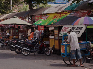 In Solo, Indonesia, the lively streets are a constant motion of tuk-tuks, motorcycles, and people, weaving through the vibrant market scene where vendors showcase their colourful goods