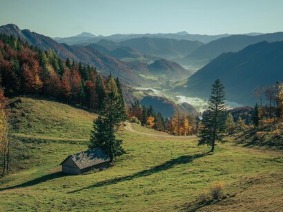 A single cabin sits in an open field surrounded by mountains, illustrating how isolation and stillness create the conditions for memory to settle