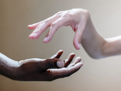 In a touching moment, the hands of two individuals gracefully clasp, bridging the space between them in a gesture of mutual support and connection