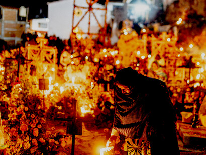 Visitors celebrate Día de los Muertos at night among glowing candles and decorated graves, honoring ancestral spirits