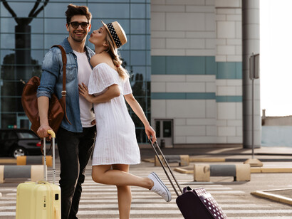 A happy brunette man embraces his girlfriend in a white dress as she welcomes him at the airport after a long distance separation