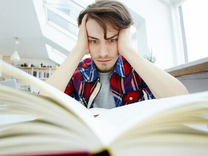 A student with OCD, sitting in the library, overwhelmed by academic stress, with their head in their hands