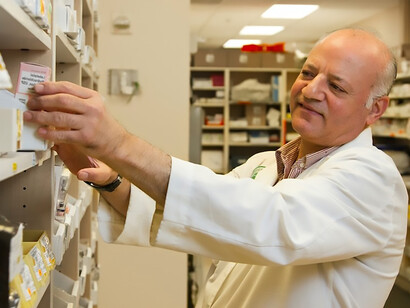 Amidst the organized shelves of a pharmacy, a conscientious male pharmacist dedicates his attention to scrutinizing a medication from the inventory
