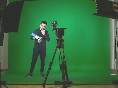 A poised individual stands confidently in front of the camera, speaking eloquently with a microphone in hand, against the backdrop of a vibrant green screen, capturing a moment of dynamic filming
