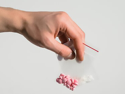 A hand holding pink and white pills in a bag