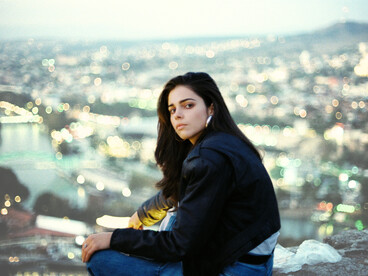 A young woman sitting on a parapet above the city, alone and looking out over the view