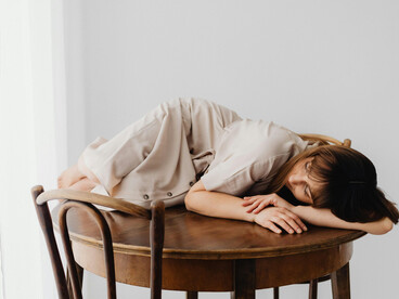 A woman leans on a table, overwhelmed, lost in her thoughts