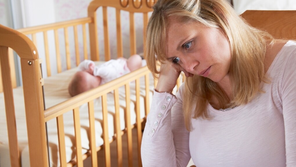 Una madre con síntomas de depresión junto a la cuna de su hijo recién nacido