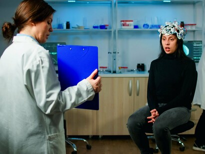 Mulher é examinada com o uso de um fone de ouvido de eletroencefalograma, dispositivo que monitora a atividade elétrica do cérebro. Essa tecnologia permite a captura de dados sobre a atividade cerebral para várias aplicações, como pesquisa, monitoramento de saúde mental e desenvolvimento pessoal. A saúde mental é uma das áreas em que a inteligência artificial tem se mostrado promissora