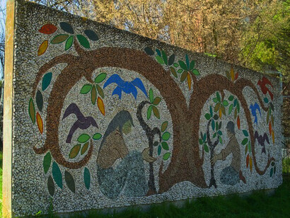 "The Tree of Life", by Deru Josette, represents life and its continuous and necessary regeneration: it depicts a tree with stylised shapes and two young people in the act of planting small shrubs. The tiles used are in limestone, granite and glass paste. The panel is large, with a horizontal development; being exposed to the elements, we can say that it is well preserved to this day