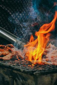 A close-up of a man grilling meat, with charcoal flames rising and adding a smoky touch to the cooking process