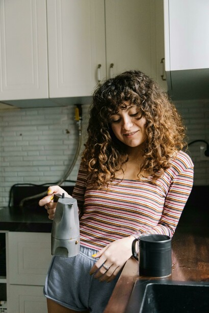 A calm kitchen scene shows a woman making coffee at home in gentle light