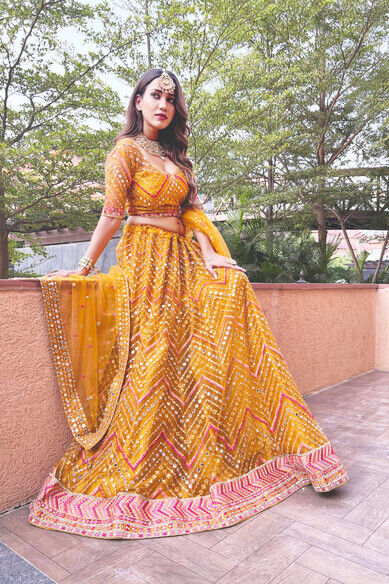 A model presents a stunning mustard yellow Phulkari lehenga embellished with intricate mirror work, zarkan, zari, and beautiful thread embroidery