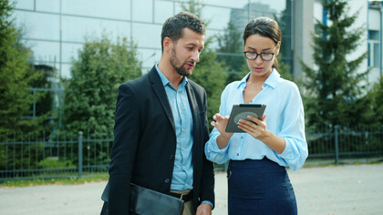 Business colleagues in business casual attire discuss work on a tablet outdoors