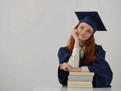 A young woman in an academic cap, freshly graduated, sits at a table smiling and posing confidently
