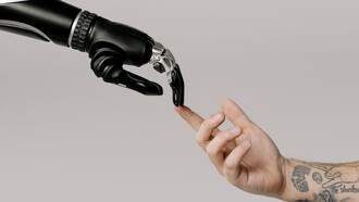 A human hand and a sleek black robot hand draw near to one another, symbolizing the convergence of human ingenuity and artificial intelligence