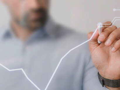 An upward-trending digital bar graph is enhanced by a businessman’s hand, symbolizing the relationship between effective leadership and economic advancement