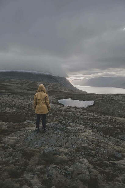 A woman stands a lone by the lake and rocks