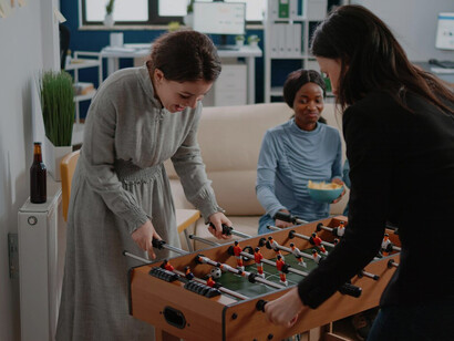Colleagues from diverse backgrounds bonding over foosball, beer, and snacks in the office, showcasing a modern shift in workplace dynamics