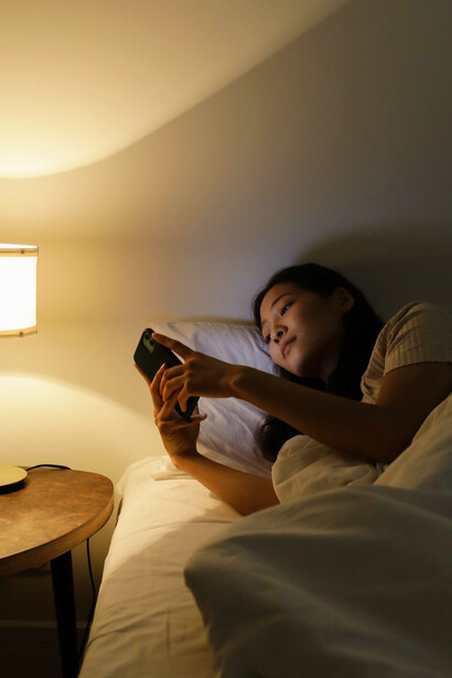 A woman lying on her bed at night, her face lit softly by the light of her phone