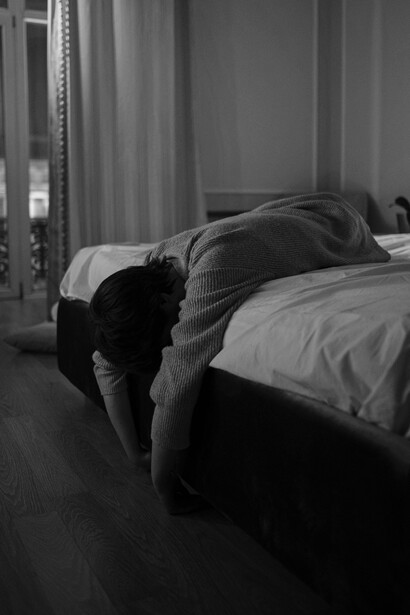 A solitary figure sits under a blanket, resting her head in her hand, reflecting a state of anxiety