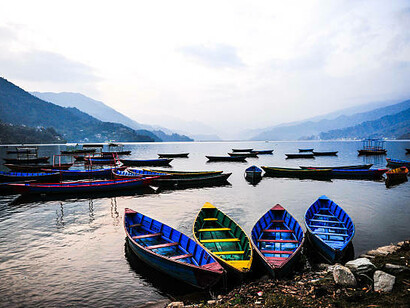 Brightly painted boats on Phewa Lake, a peaceful freshwater lake in Nepal’s Pokhara Valley, framed by the landscapes of Pokhara, Sarangkot, and Kaskikot
