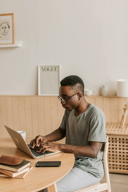 A man in a gray shirt works on academic writing using his laptop