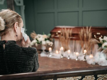 A grieving woman stands beside a flower-adorned coffin during a funeral service
