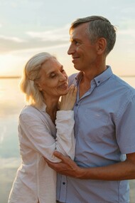 A sweet couple standing by the water at sunset, sharing a peaceful moment together