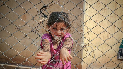 A young girl grips a chain-link fence in Idlib, Idlib Governorate, Syria