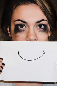 A woman, initially in tears, now holds a paper with a smiley face in front of her, symbolizing her changing emotions and resilience