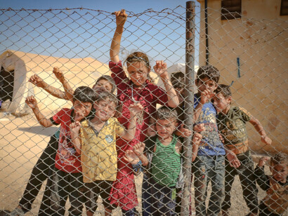 A group of young children standing closely together behind a chain-link fence