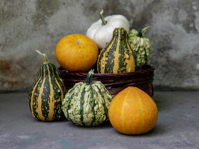 Different types of gourds and pumpkins on a concrete floor next to a wooden clock