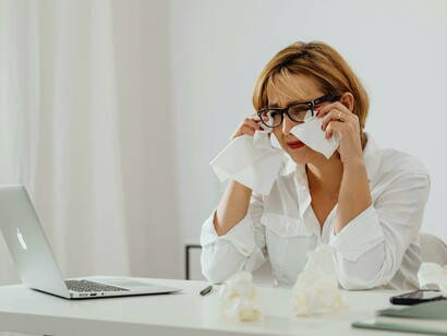 A stressed woman wearing white long sleeves is visibly crying at her workplace